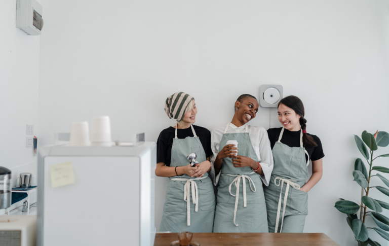 three standing waitresses leaning against clean white wall enjoying a coffee on their break. 