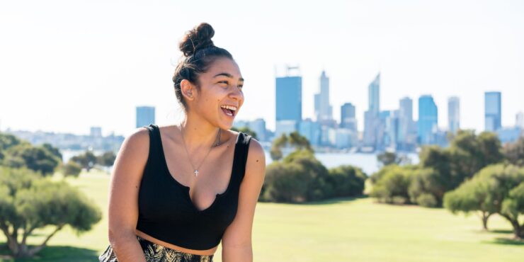 A woman is pictured laughing in front of a park with a cityscape in the background
