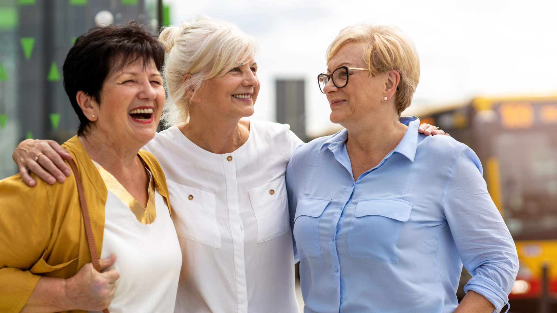 Three senior women are smiling and laughing as they have their arms around one another