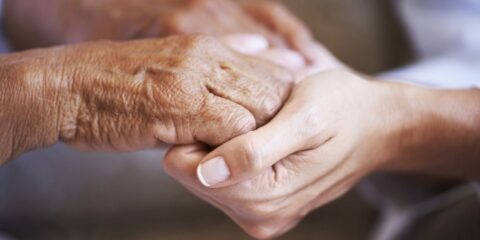 An elder person's hand is gripped by a younger appearing hand