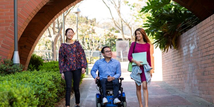 Two women and a man in a mobility scooter walk across Curtin's Bentley campus