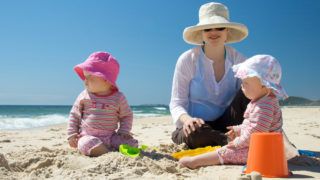 A mother and her twin girl babies enjoy a day at the beach while being sun-smart.