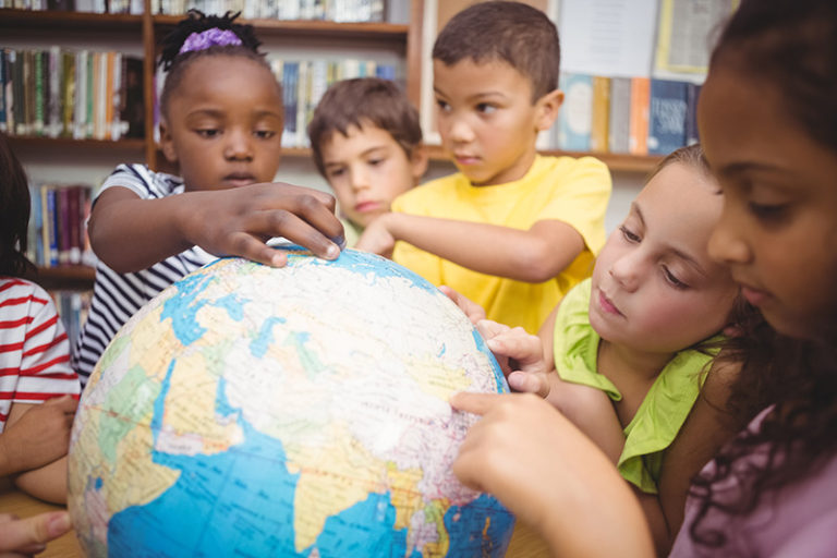 Primary school aged children pointing at countries on a world globe