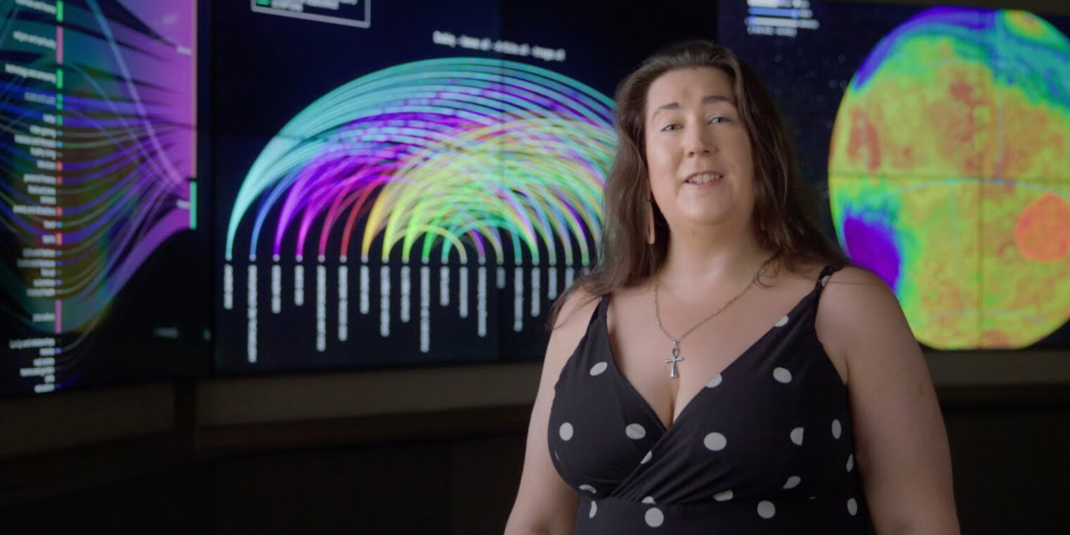 Professor Melanie Johnston-Hollitt standing in front of large data-visualisation screens - play video