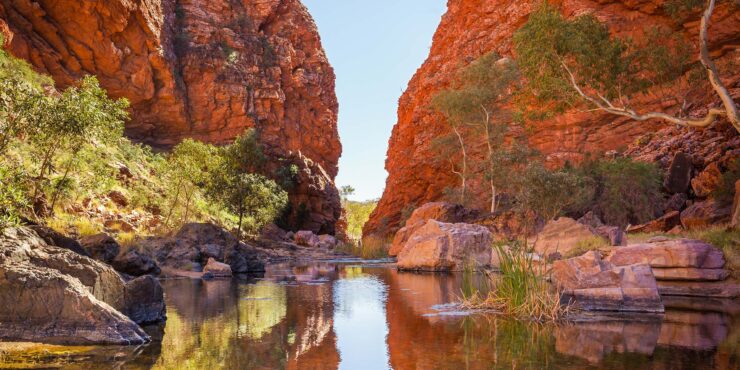 Picturesque view of the Australian outback, with large red natural rock structures, trees and water